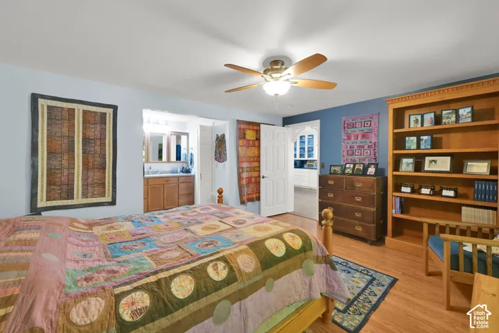 Wood-finish flooring, built-in floor-to-ceiling shelving, ceiling fan with light fixture, and a vanity featuring wood cabinetry