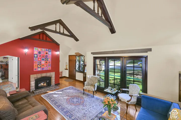 Vaulted ceiling featuring exposed decorative trusses, wood-finish flooring, masonry fireplace with a mantel, and multi-pane glass doors
