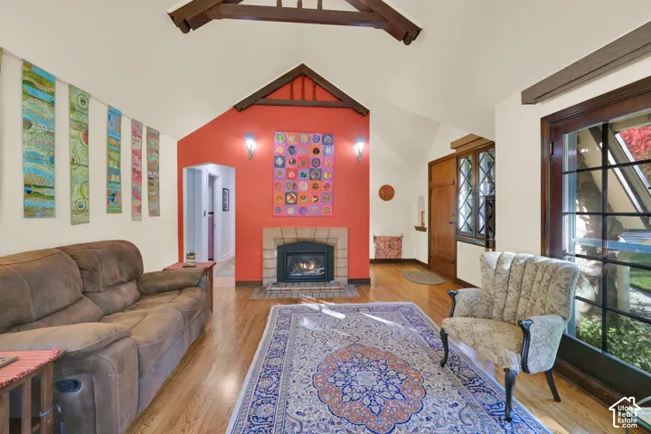 Vaulted ceiling with exposed decorative wood trusses, wood-finish flooring, masonry fireplace with tile surround, and diamond-pane window detailing