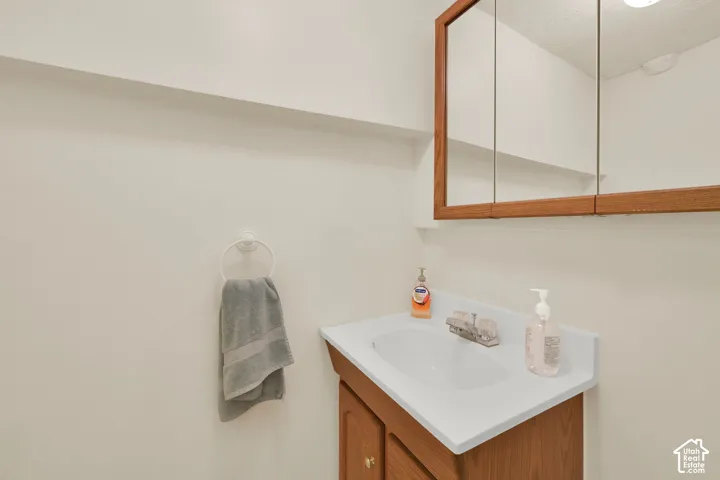 Bathroom vanity featuring a wood-finish cabinet, integrated countertop basin, metallic faucet, and tri-fold mirrored medicine cabinet