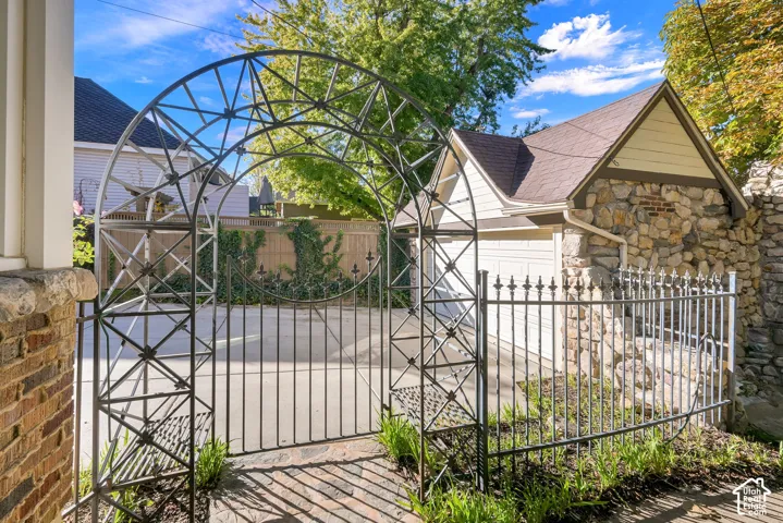 Decorative metal arched gate with integrated fencing, stone masonry garage exterior, and concrete driveway
