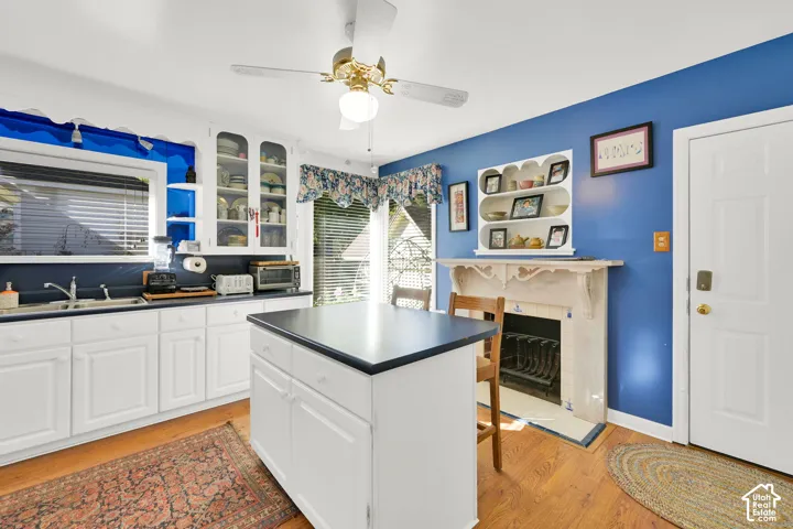 Kitchen featuring white cabinetry, center island with dark countertop, built-in display shelving, hearth with decorative mantle, and wood-finish flooring