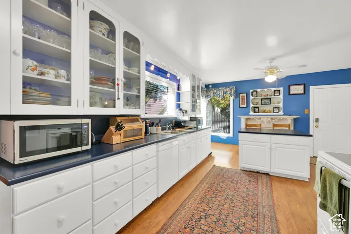 Kitchen featuring white cabinetry with glass-front uppers, solid-surface countertops, wood-finish flooring, and a built-in island