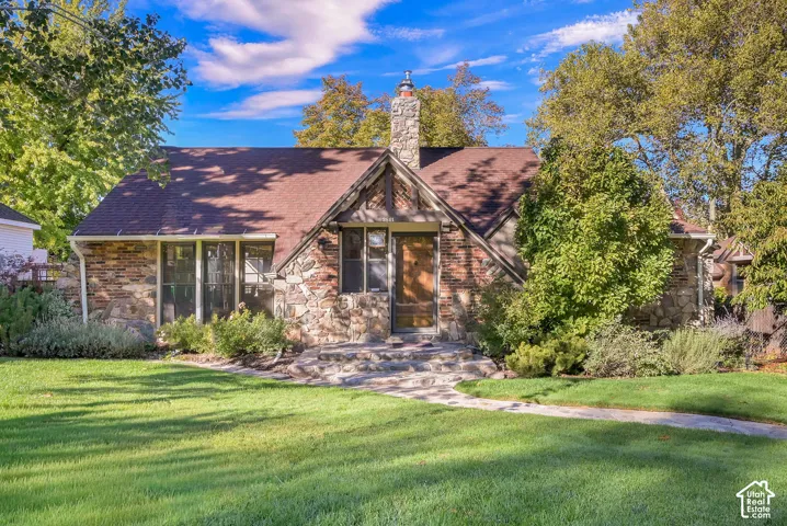 Stone exterior facade with timber-framed accents, steeply pitched roof, prominent stone chimney, and flagstone walkway