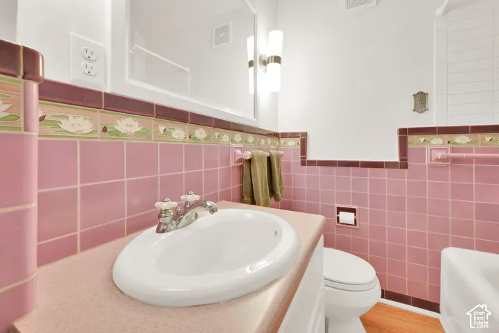 Wall-mounted vanity featuring a solid surface countertop, drop-in sink with dual-knob faucet, custom floral tile backsplash, and dual-light sconce