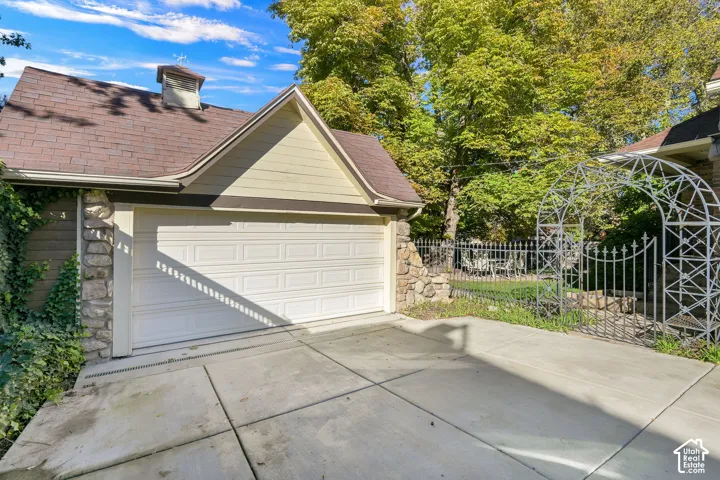 Detached garage with stone masonry accents, shingled roof, cupola, and metal garden arbor