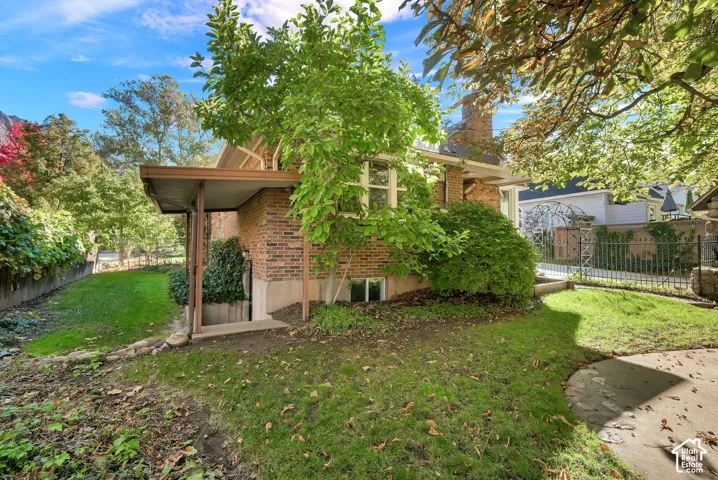 Brick exterior featuring a covered side entryway, foundation-level window, mature landscaping, and metal perimeter fencing