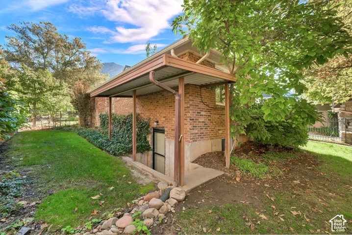 Exterior brick structure featuring a covered basement entryway, concrete foundation, and landscape perimeter with stone hardscaping
