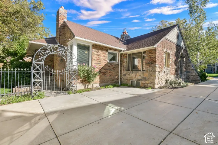Brick and stone masonry exterior featuring an arched metal garden gate, a concrete driveway, and multiple bay windows