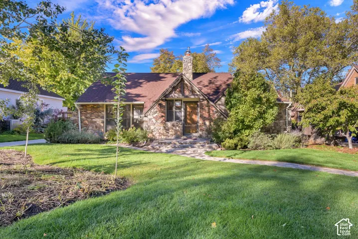 Tudor-style exterior featuring stone cladding, half-timbering accents, a prominent stone chimney, and a stone walkway