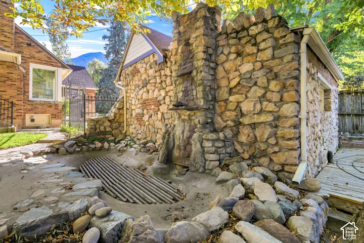 Exterior stone masonry wall featuring an integrated stone chimney, decorative stone ornamentation, and a concrete-lined water feature with a metal grate cover