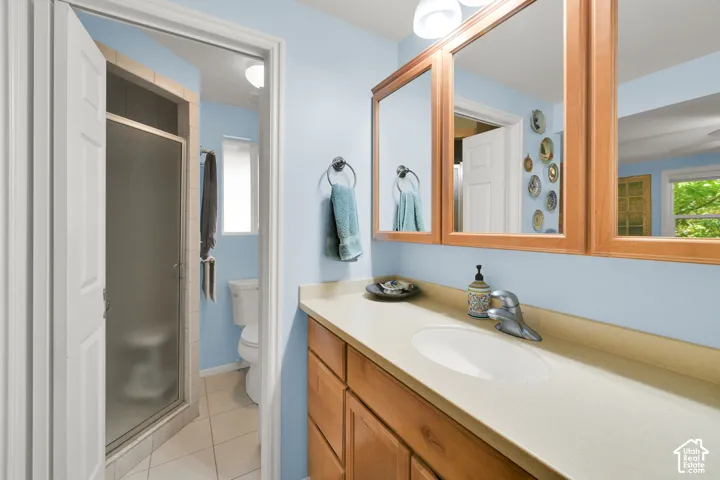 Bathroom featuring a single-sink vanity with solid-surface countertop, wood-finish cabinetry, framed tri-fold medicine cabinet, and glass-enclosed shower