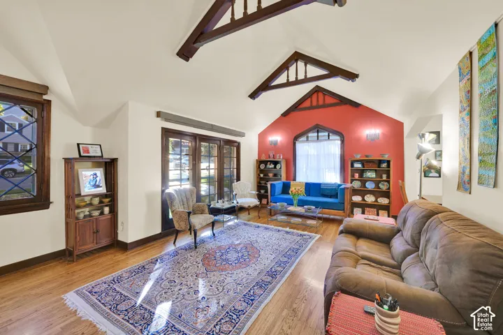 Living area featuring vaulted ceilings with exposed wood trusses, wood-finish flooring, a pointed-arch window, and multi-pane wood-frame exterior doors