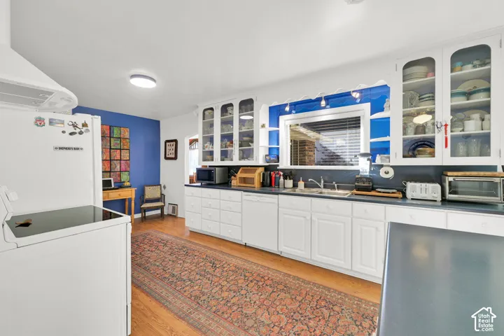 Kitchen featuring white cabinetry, glass-front display uppers, wood-finish flooring, a double-basin stainless steel sink, and a range hood