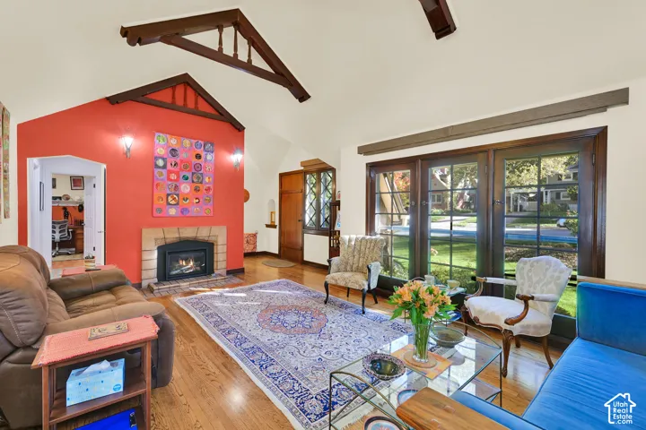 Vaulted ceilings featuring exposed timber trusses, wood-finish flooring, masonry fireplace, and multi-pane French doors with dark wood trim