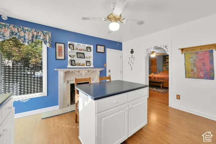 Wood-finish flooring, fireplace with ornate mantle, built-in shelving, white cabinetry, and ceiling fan