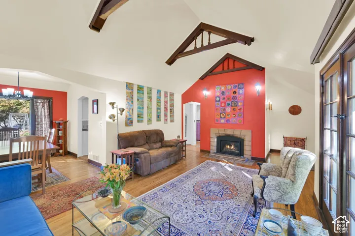 Vaulted ceilings with exposed decorative wood trusses, hardwood flooring, fireplace with a tiled surround, and multi-pane glass doors