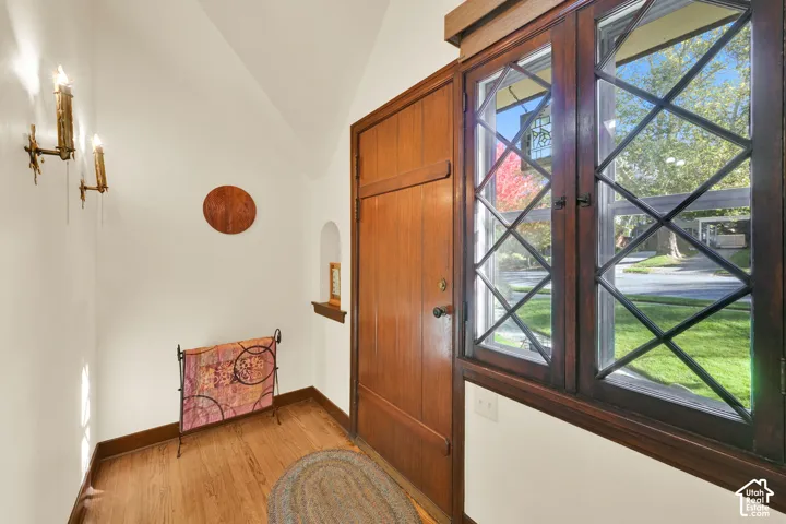 Solid wood door with dark hardware, diamond-pane lattice windows with wood casing, arched wall niche, and dual wall-mounted candle-style light fixtures