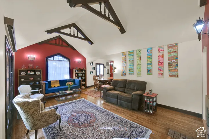 Vaulted ceiling featuring exposed decorative trusses, wood-finish flooring, and arched window frame