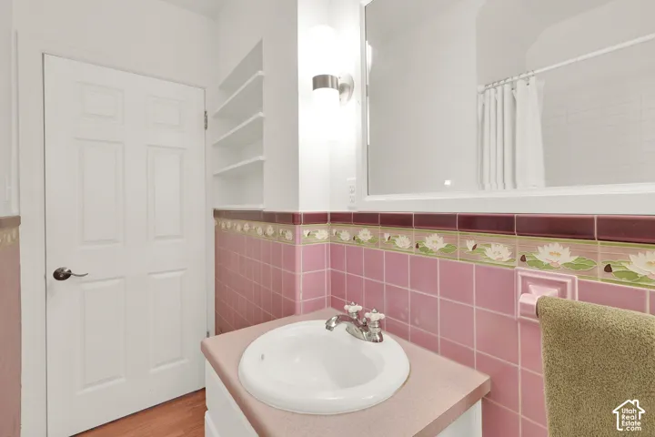 Bathroom featuring decorative ceramic tile wainscoting with floral accents, built-in wall shelving, integrated countertop sink, and wall-mounted light fixture