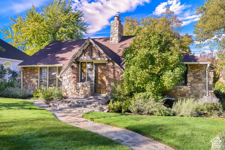 Tudor-style exterior featuring stone cladding, a prominent stone chimney, timber-accented gable, and a curved natural stone walkway