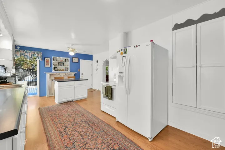 Kitchen featuring wood-finish flooring, white cabinetry, an island with a dark countertop, built-in shelving, and a white refrigerator