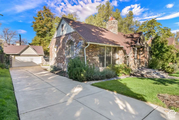Exterior featuring a blend of brick and natural stone masonry, steep-pitched roofline, stone chimney, detached garage, and concrete driveway