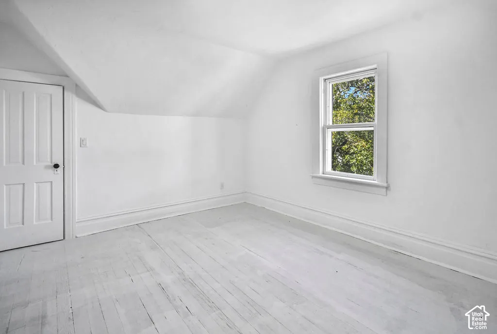 Room featuring wood-finish flooring, a sloped ceiling, and a single-hung window with exterior tree foliage