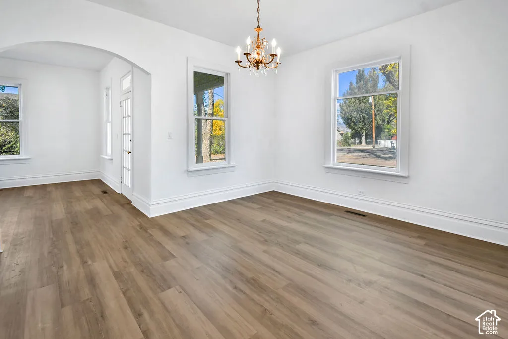 Interior space featuring wood-finish flooring, a multi-arm candelabra-style chandelier, arched architectural detailing, and large windows with exterior casing