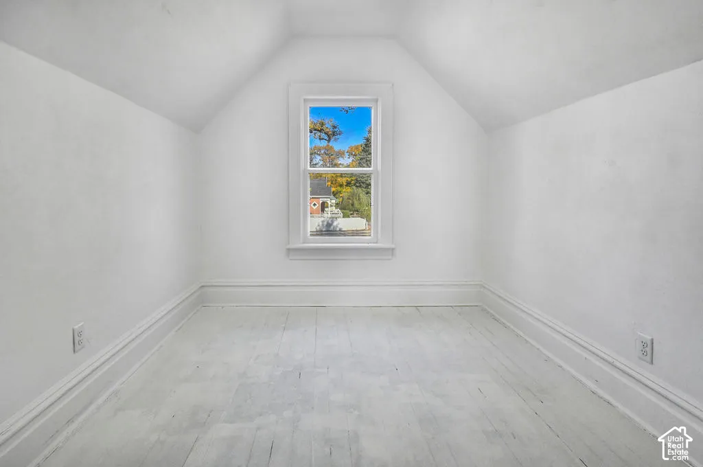 Room featuring vaulted ceilings, wood-finish flooring, and a central window with exterior scenery