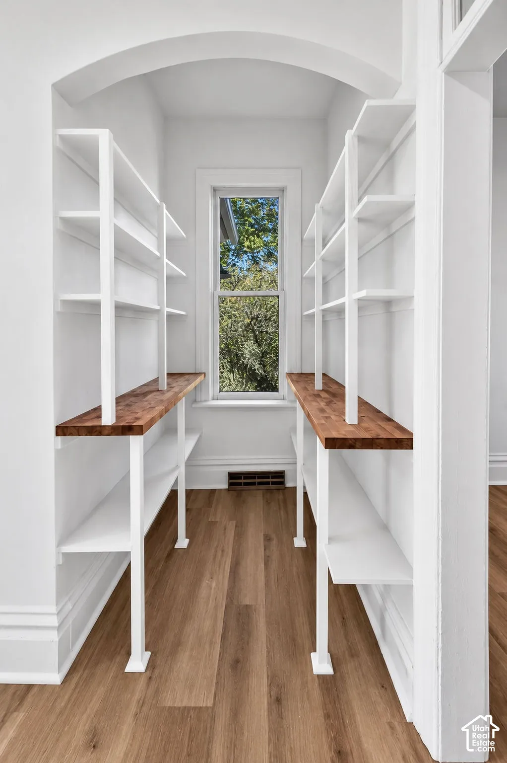 Built-in shelving featuring white metal supports, wood-finish countertops, wood-finish flooring, and an arched entry