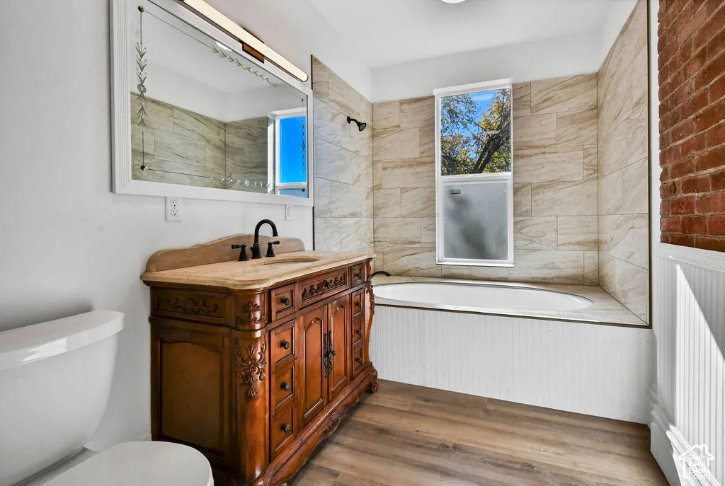 Bathroom featuring an ornate wooden vanity with a stone countertop, undermount sink, matte black faucet, and an exposed brick accent wall