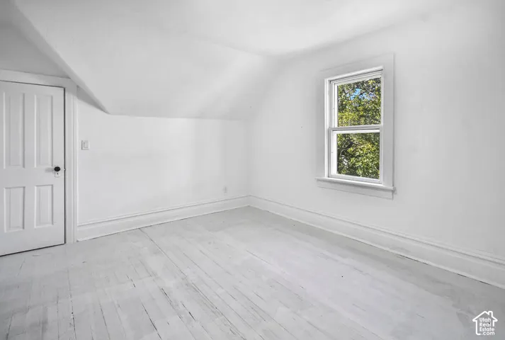 Room featuring wood-finish flooring, a sloped ceiling, and a single-hung window with exterior tree foliage