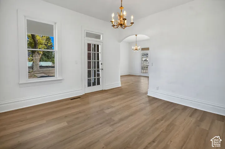 Interior space featuring wood-finish flooring, two multi-pane glass doors with transom windows, arched architecture, and traditional chandeliers