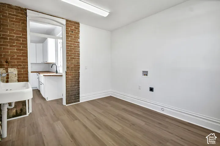 Exposed brick wall accent, wood-finish flooring, and wall-mounted utility sink