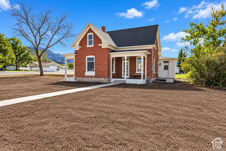 Brick exterior featuring a covered front porch, stone foundation detailing, and a concrete walkway
