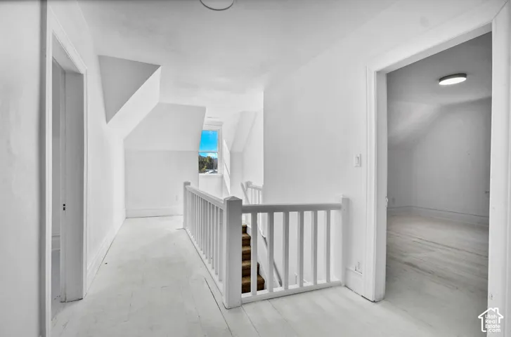 Staircase featuring a white-painted wooden balustrade, wood-finish flooring, vaulted ceilings, and a window with mountain scenery