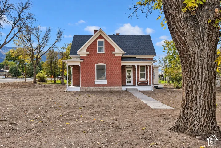 Traditional red brick exterior featuring a steep-pitched gable roof, covered front porch with decorative posts, and a stone foundation