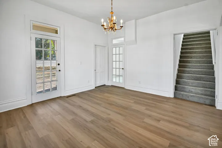 Wood-finish flooring, multi-pane glass doors with transom windows, overhead candelabra-style chandelier, and carpeted staircase