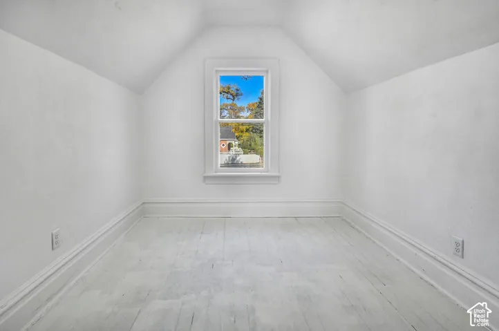 Room featuring vaulted ceilings, wood-finish flooring, and a central window with exterior scenery