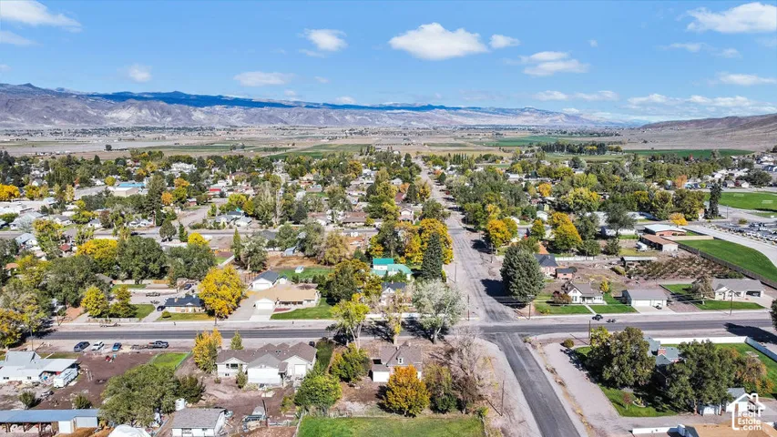 Aerial perspective of the residential area featuring mature trees, paved roadways, and a backdrop of expansive mountain ranges