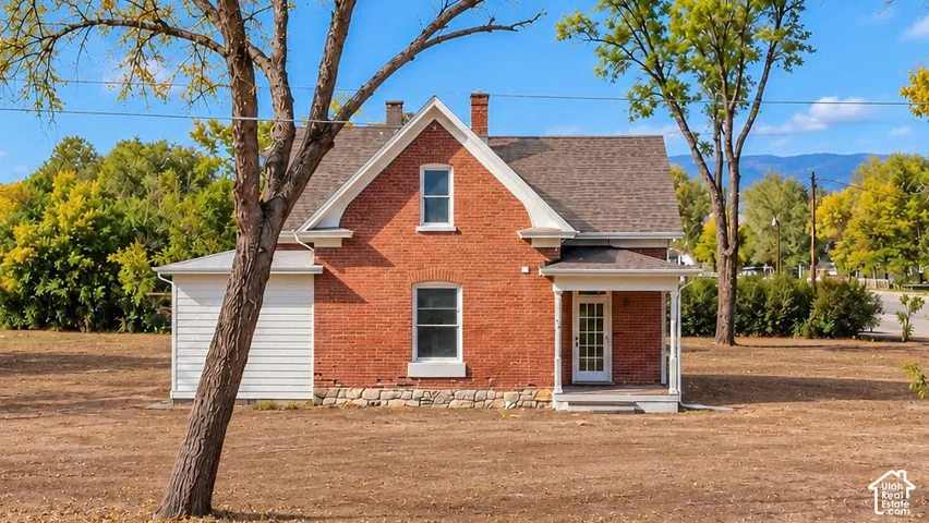Red brick exterior featuring a stone foundation, a covered front porch with white columns, and a peaked roofline