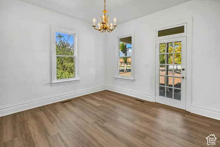 Interior space featuring wood-finish flooring, multi-pane windows with white casing, a decorative brass chandelier, and a glass-paneled exterior door with a transom window