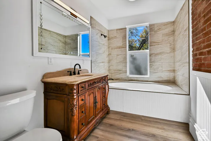 Bathroom featuring an ornate wooden vanity with a stone countertop, undermount sink, matte black faucet, and an exposed brick accent wall