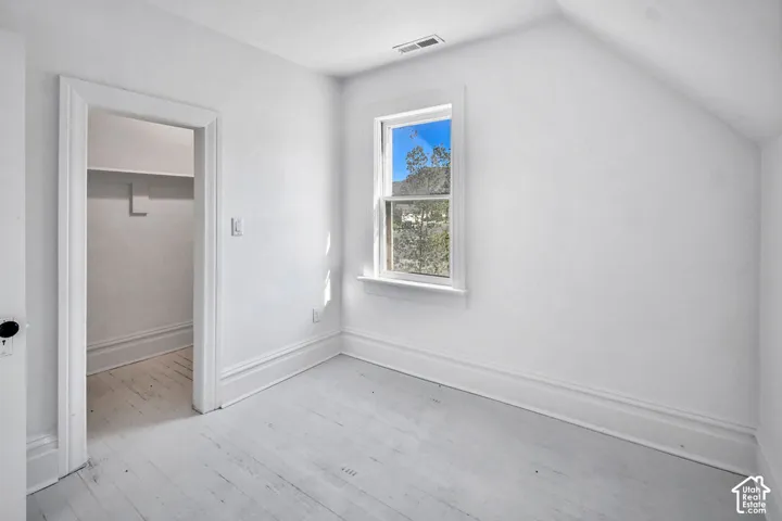 Painted wood flooring, neutral wall finishes, single-hung window with natural light, and walk-in closet with built-in shelving