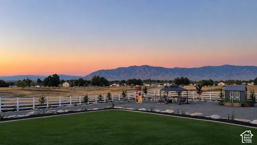Fenced backyard featuring a manicured lawn, stone hardscaping, a metal-roof gazebo, and a storage shed, set against a mountain backdrop