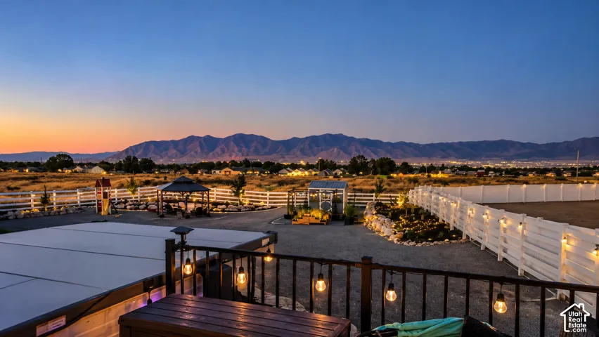 Expansive outdoor space featuring a fenced perimeter, stone-ground landscaping, a permanent gazebo, a dedicated greenhouse structure, and mountain backdrop