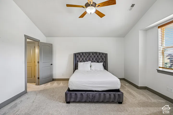 Vaulted ceiling with an integrated wooden ceiling fan, neutral carpeting, and oversized window with horizontal blinds