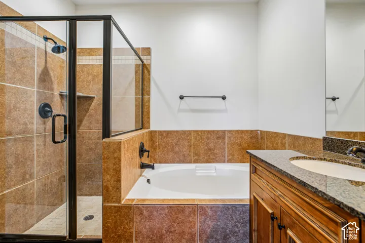 Bathroom featuring a glass-enclosed shower with tile surround, a deep soaking tub, and a wood vanity with a stone countertop and integrated sink