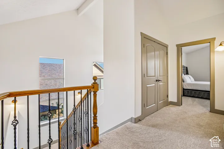 Vaulted ceilings, staircase featuring a stained wood handrail with decorative metal balusters, and neutral carpeting